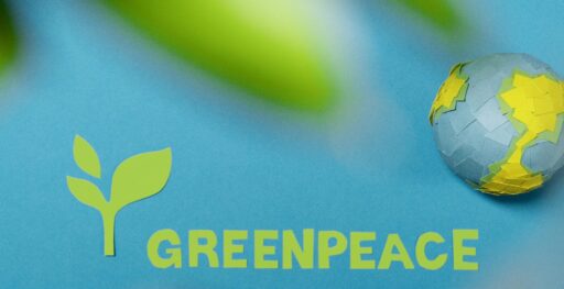 Greenpeace logo and Earth cutout on blue background symbolizing environmental awareness.